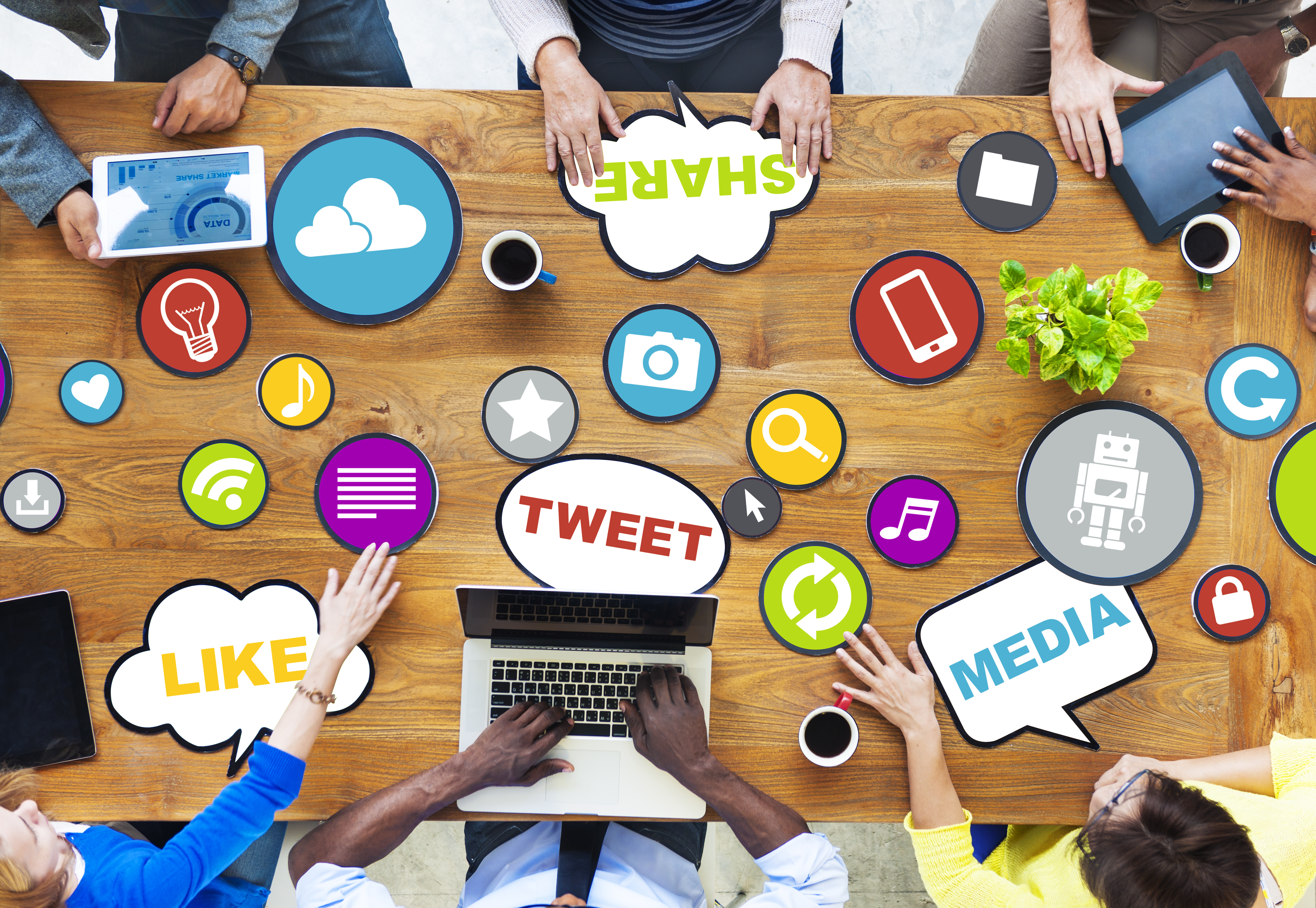 People at a table using laptops and tablets surrounded by images representing social media. 